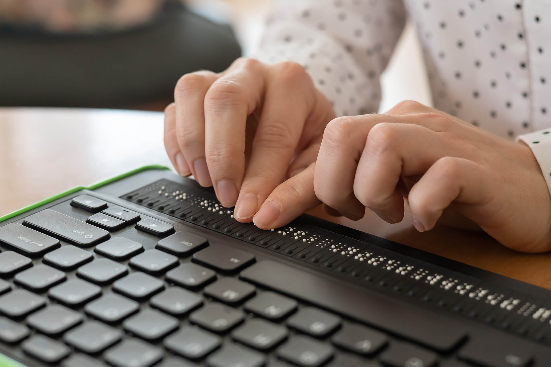 A woman uses a computer with a Braille display and a computer keyboard