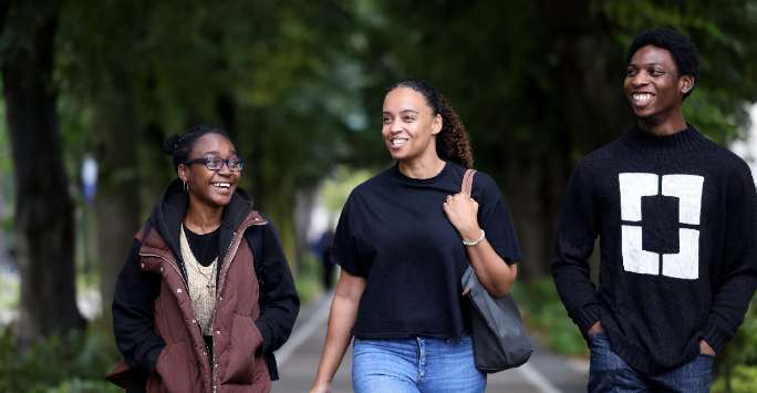 Three students walking towards the camera, smiling and laughing with one another