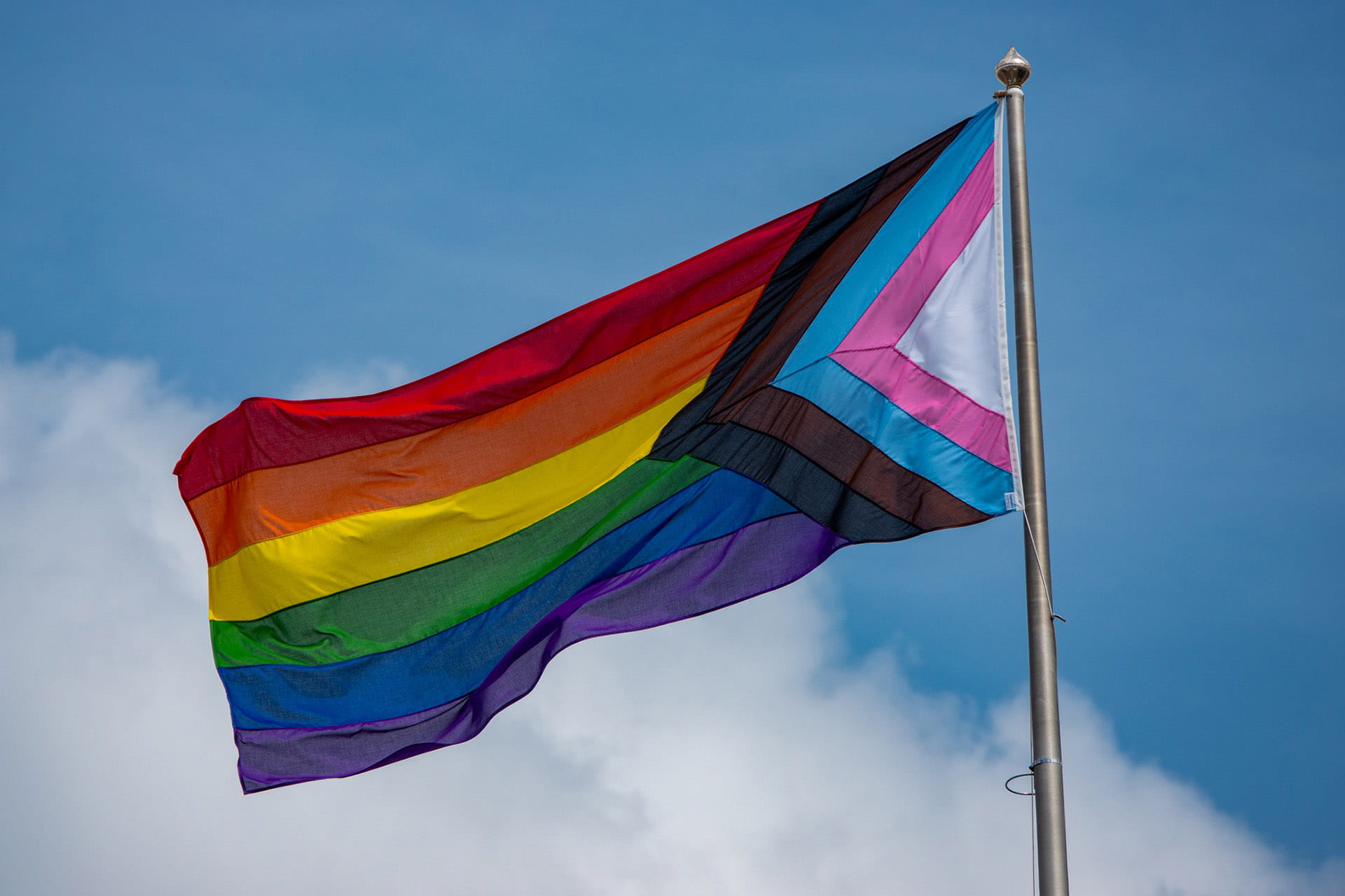 Progress pride flag flying against a blue sky