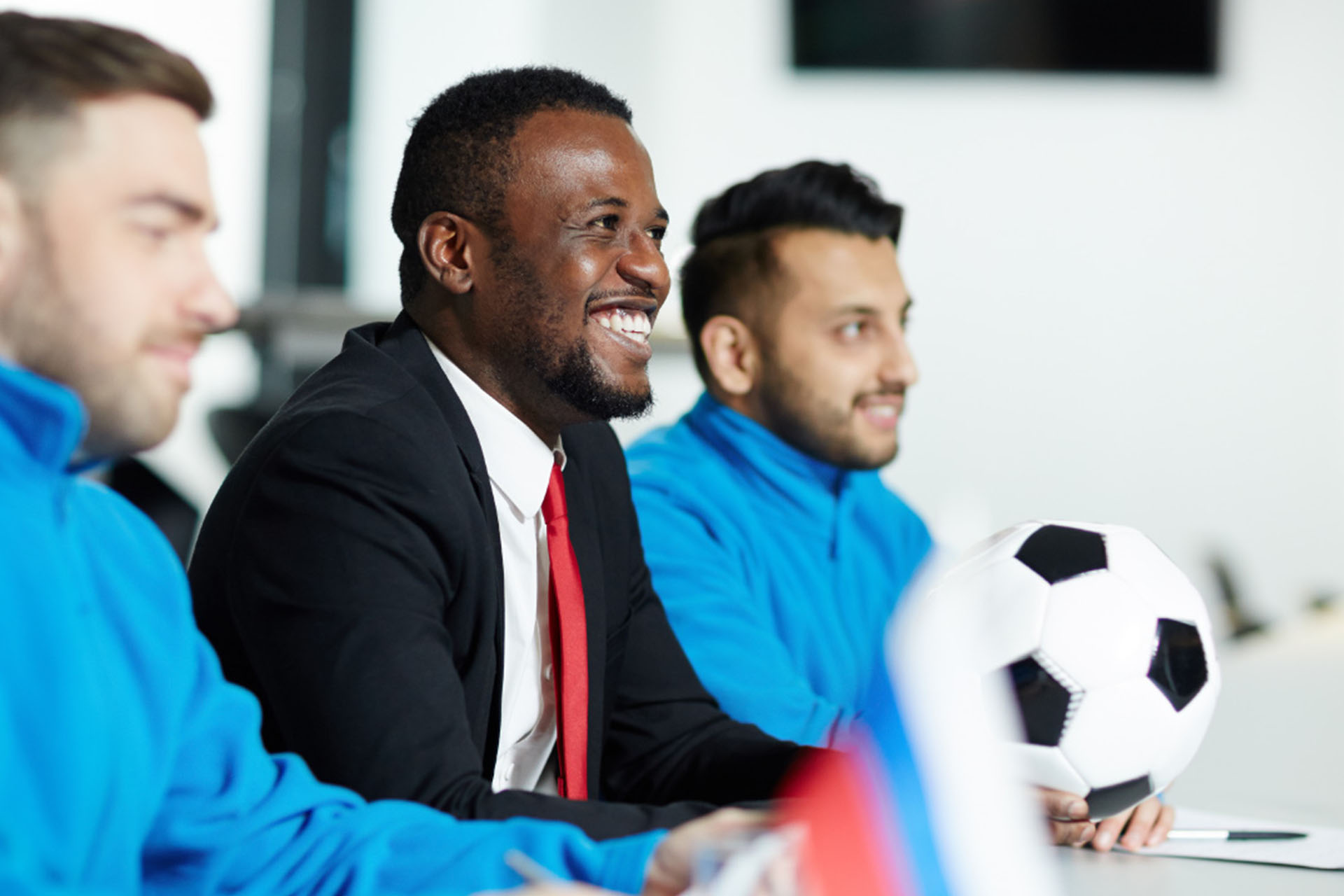 Two white male football players sitting at a table with a black male football manager