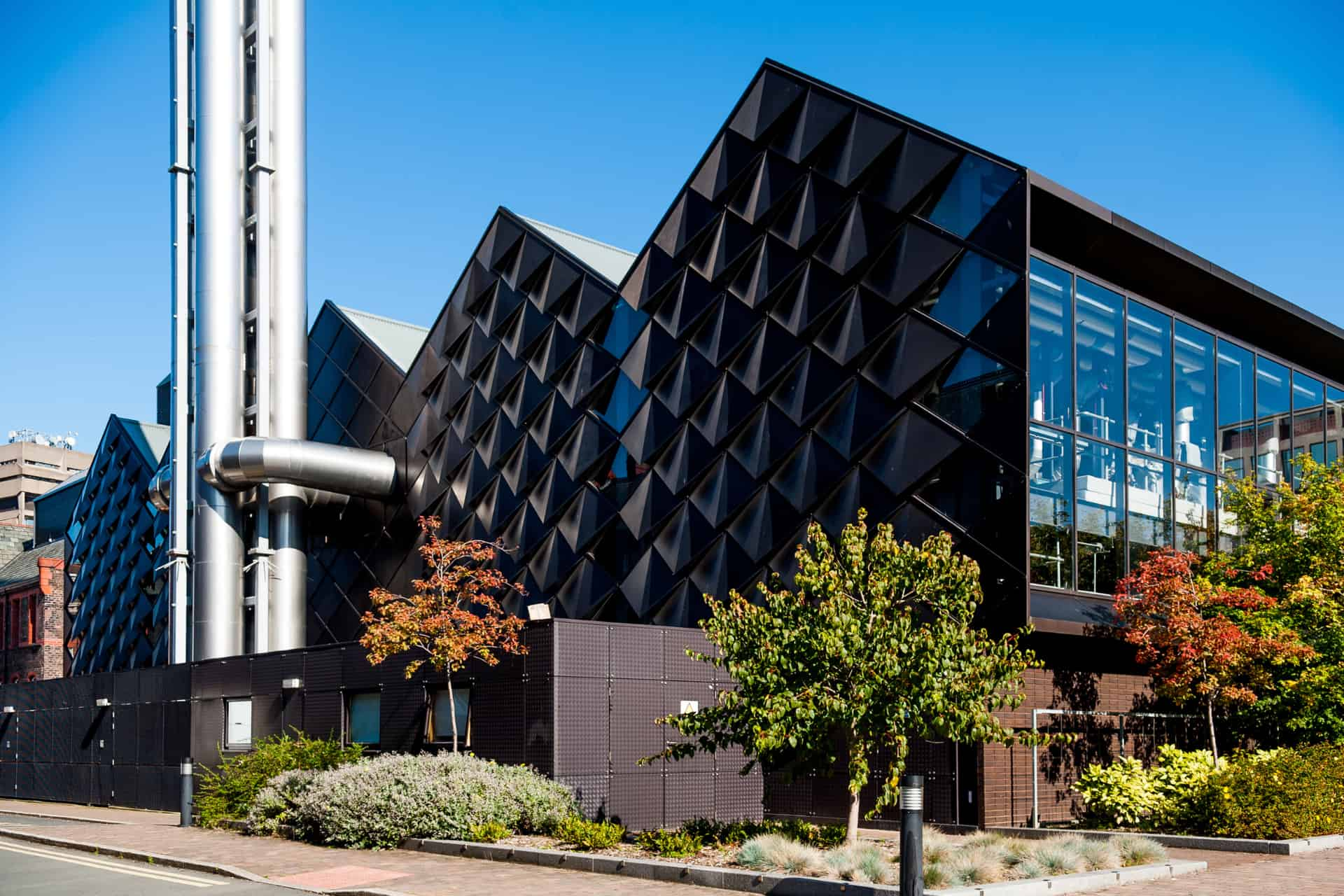 A metalic building with triangular spikes on one side and large pipes jutting into the sky.