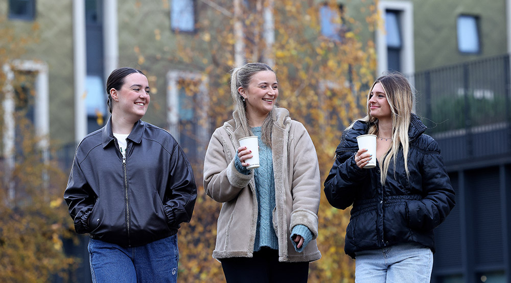 three students walking with a hot drink in hand