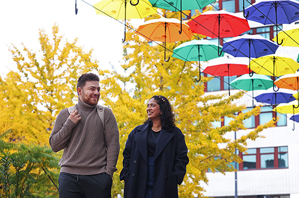 Two students walking across campus under an installation of colourful umbrellas