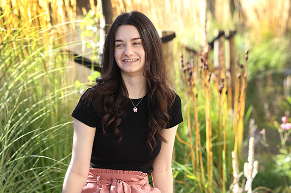 Student sitting on a bench with plants and trees behind them