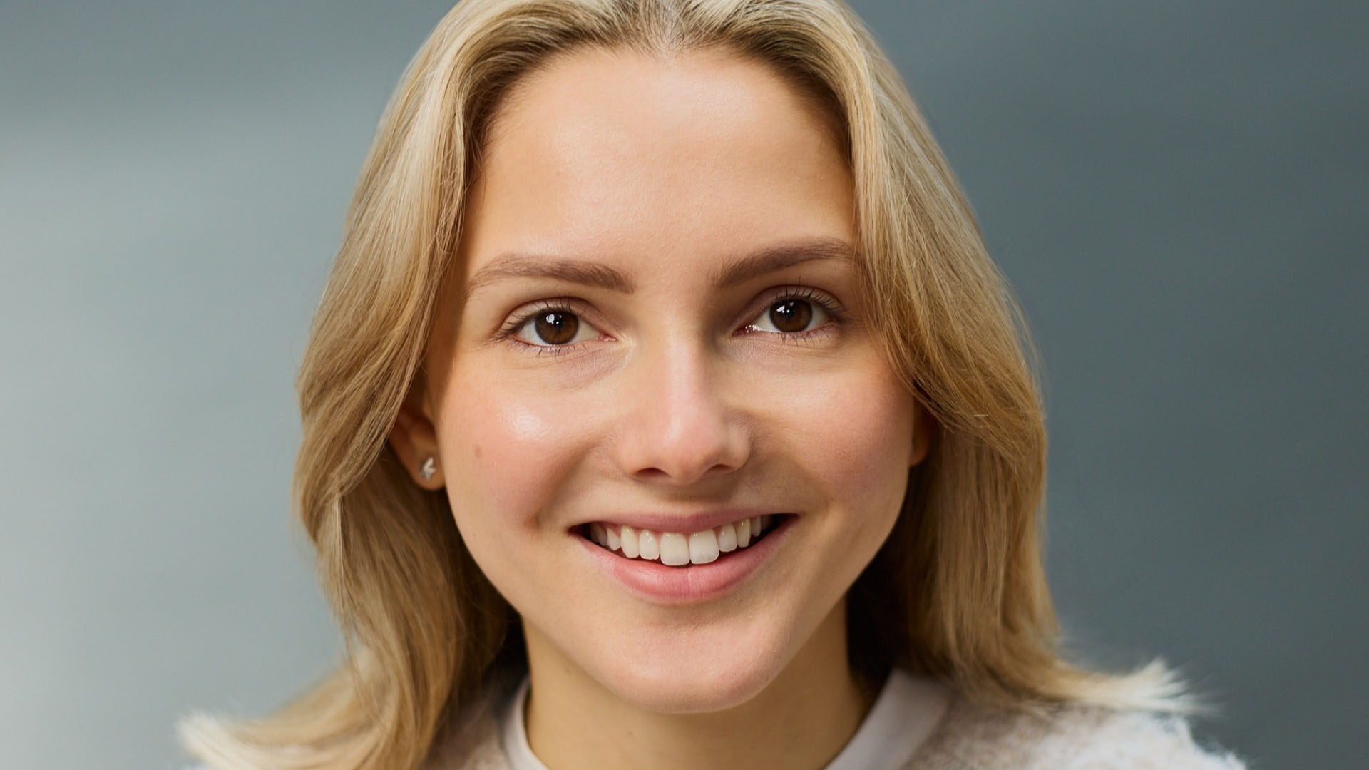 Professional headshot of someone smiling at the camera with a blue background