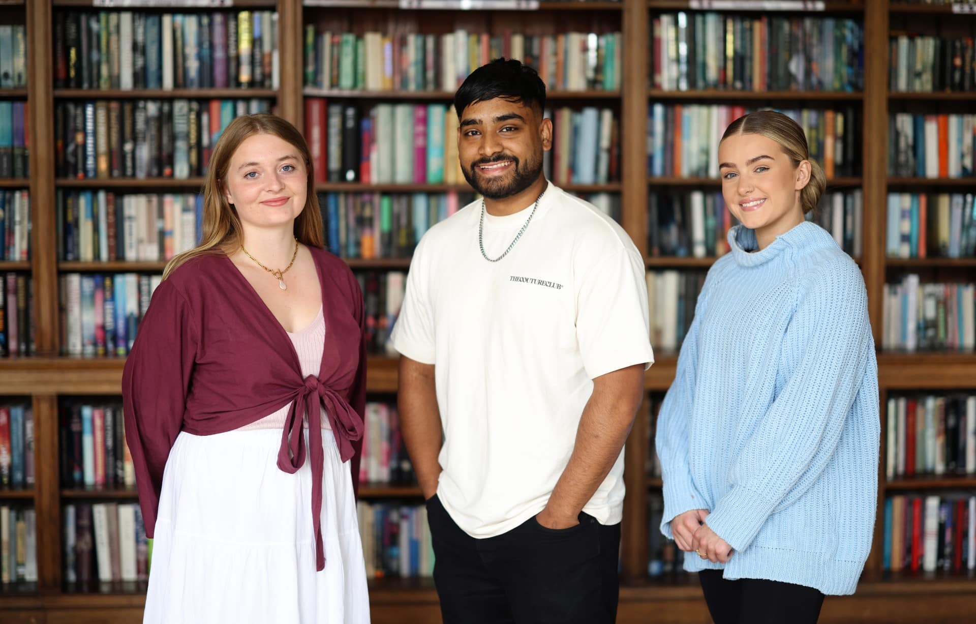 Three students in front of library of books