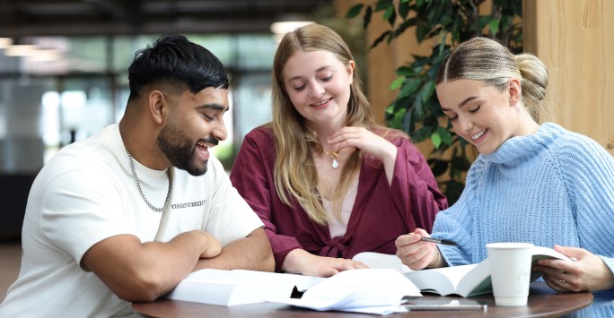 Three students sat at a table looking at a book