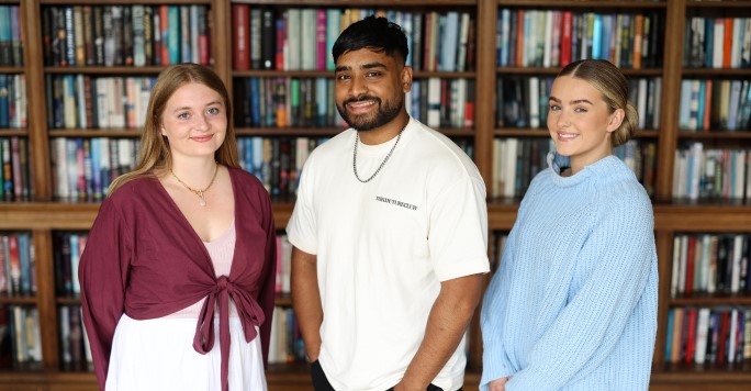 Three students standing in front of a library of books