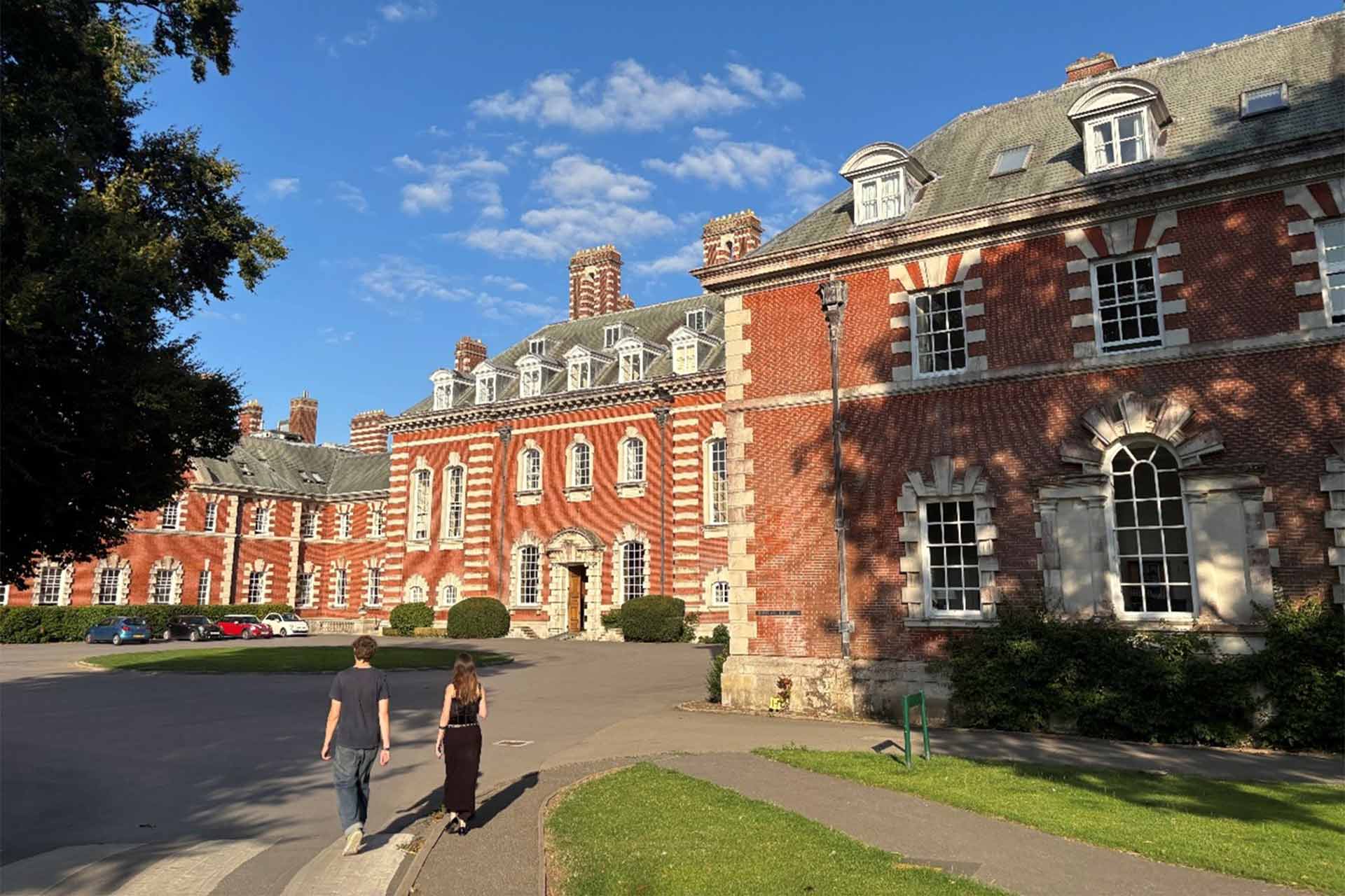 A large english stately home and estate with trees and a tarmaced front.