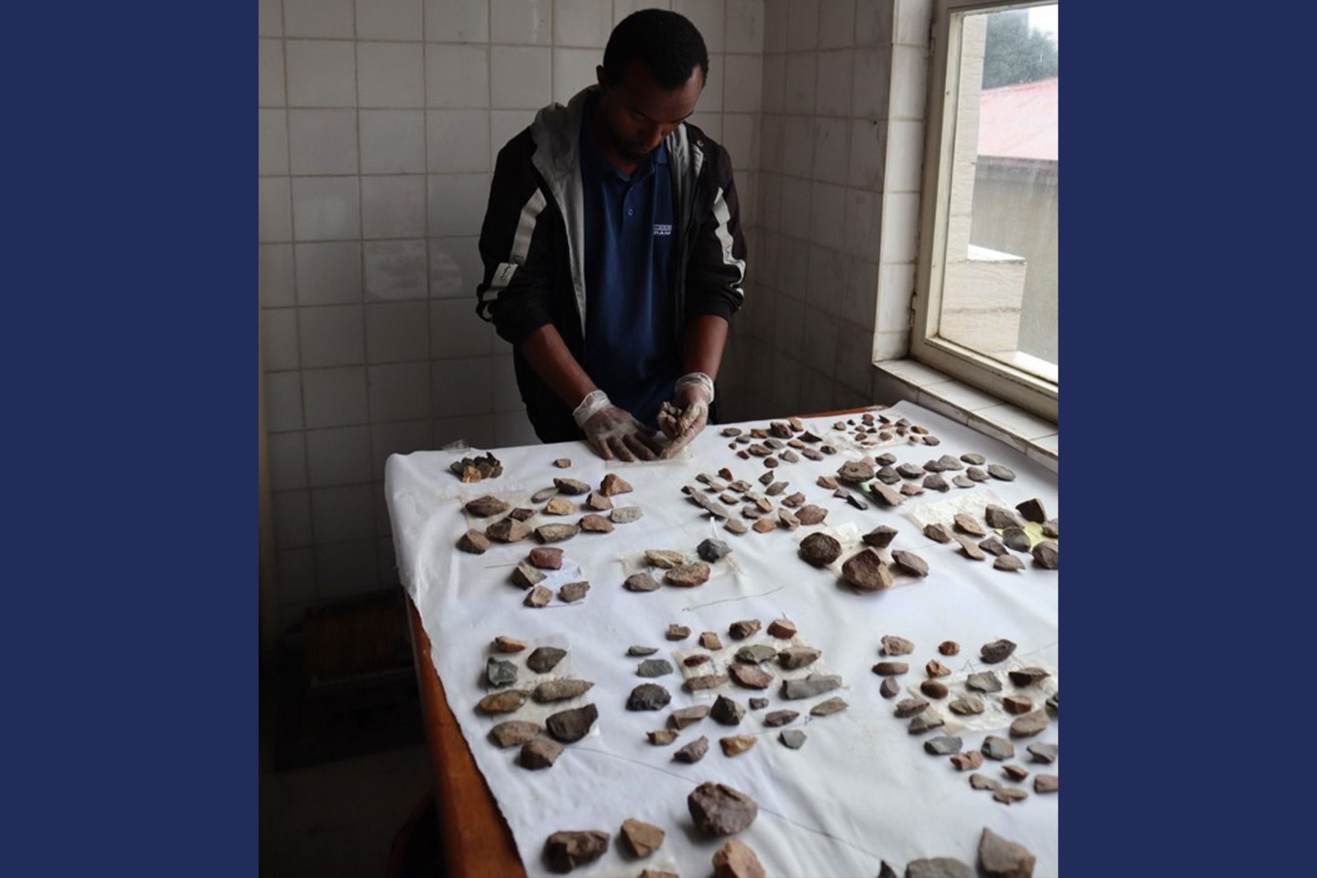 A man stands over a table with ancient stone artefacts grouped into small piles