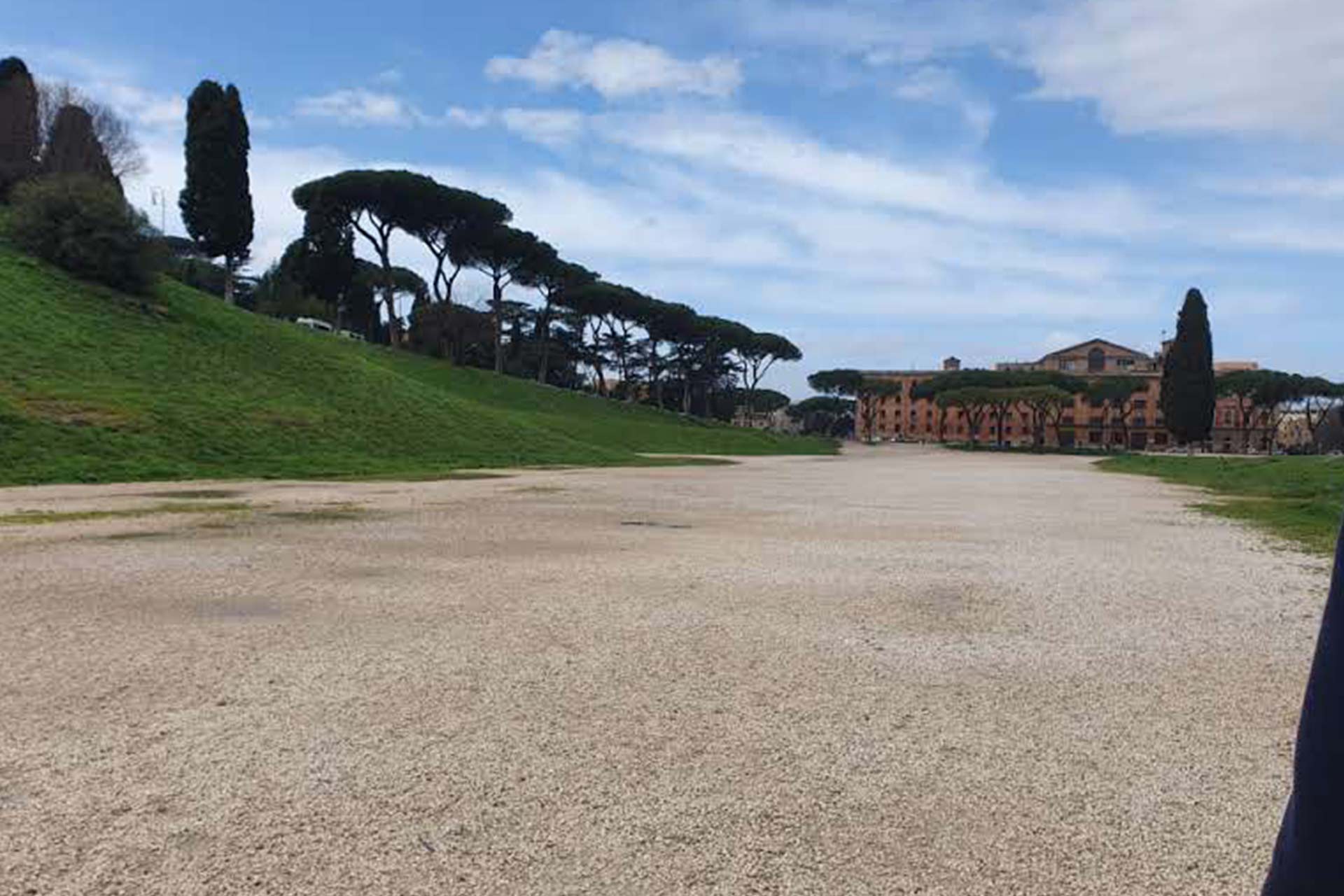 A grassy mount on the left, a sand path leading up to a large building in the distance