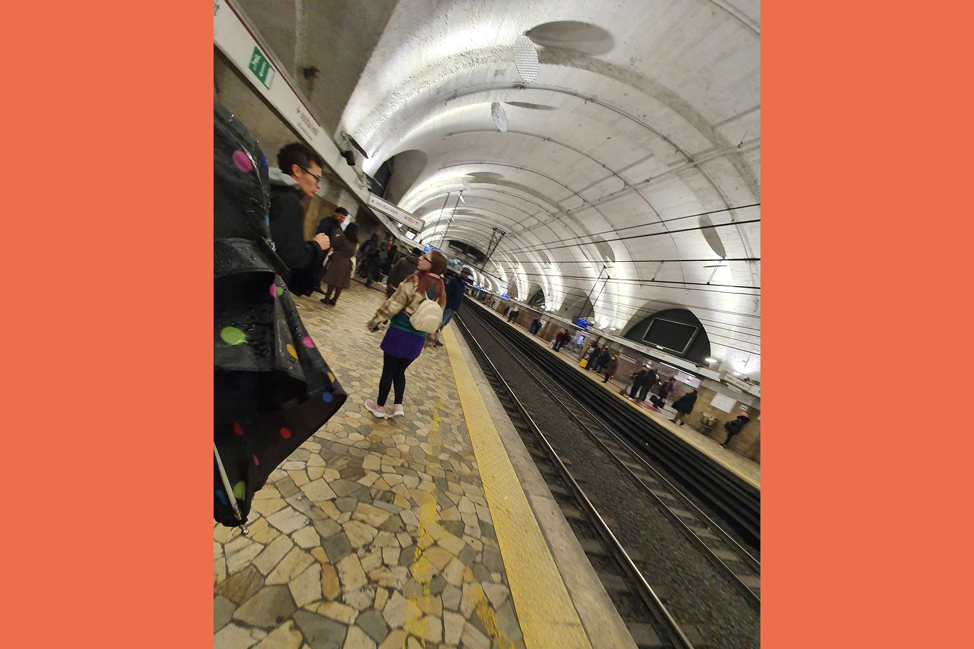 The inside of a train station, the roof is domed and white and people are waiting on the platform