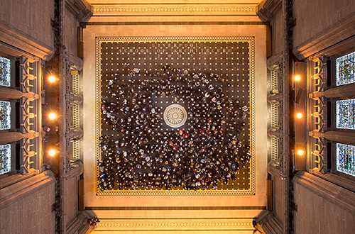 Large group of people standing on a marble floor under a cathedral tower.