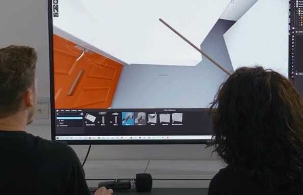 A man and a woman sitting in front of a large computer monitor studying an empty room displayed on the screen.