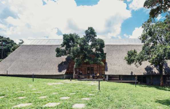 Grassed mound with a path to a building with a pitched roof and a large tree at the entrance.