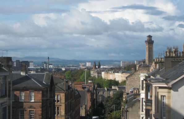 View across the slated rooftops of a Scottish city, a shipbuilding crane is visible in the background, hills are visible on the horizon.