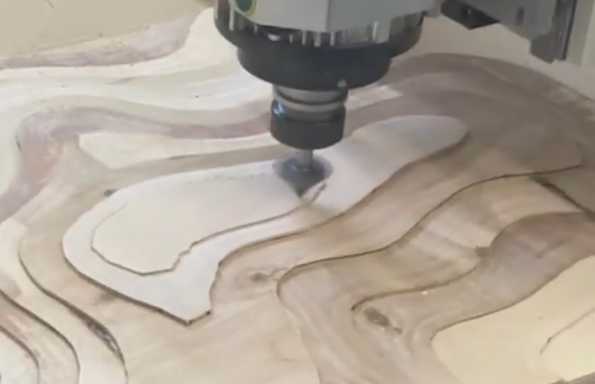 Close up of a wooden contour model being milled by a drill bit attached to a CNC machine.