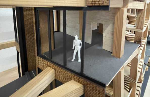 Wood and plastic cutaway model of a multi story building. On one floor is a small scale model of a person.