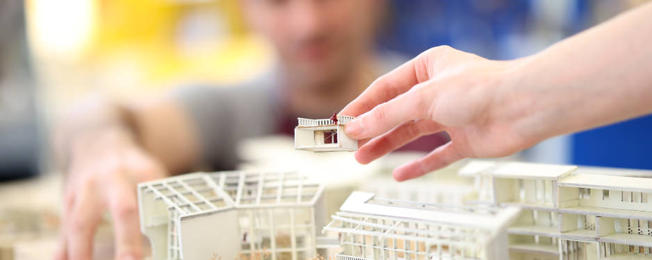 Hand holding a small model of a building element over a model.