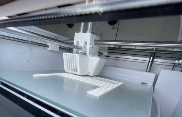 head of a 3D printer printing a building model element in white plastic.