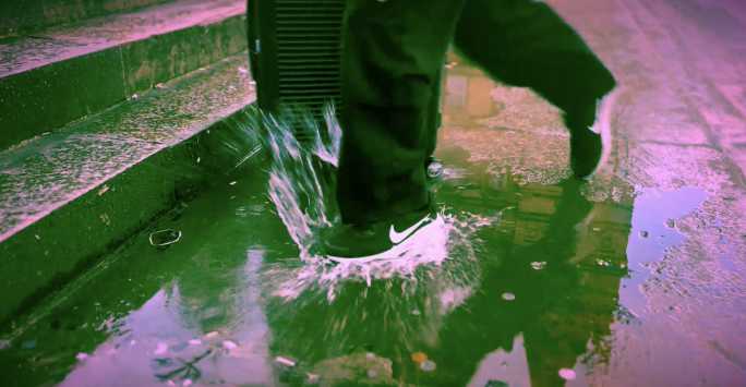 Colour graded shot of a suitcase with a foot splashing in a puddle.