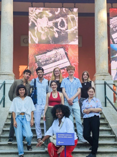 A group of young people standing on a stone staircase, two columns are behind them at the top.