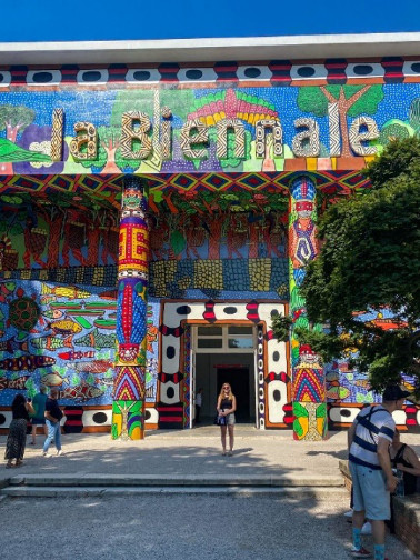 A woman standing between two columns at the door to a building. The walls and columns are decorated in a south american style.