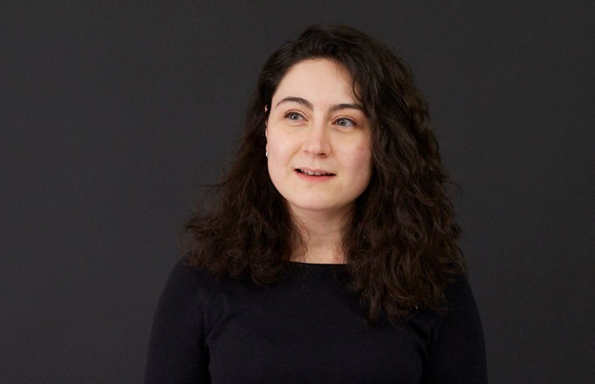 Young woman with shoulder length curly hair wearing a black jumper.