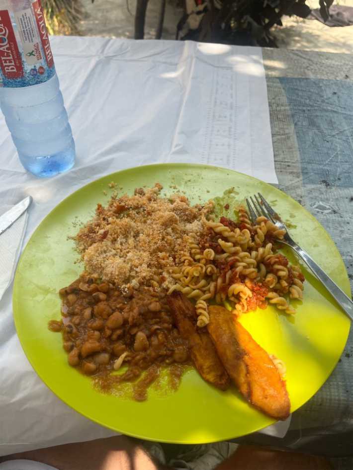 Table outdoors with a tablecloth and plate. On the plate are beans, and pasta.