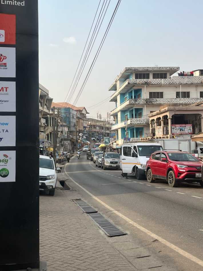 Busty Ghanan street with cars and low office blocks and cables running from one side of the street to another.