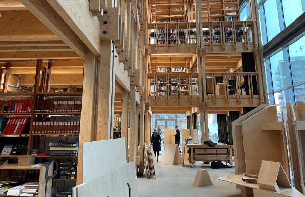 Long view of a corridor in a library. There are banks of books on wooden shelves surrounded by heavy wooden structural elements of the building.