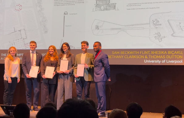 A woman and five men stand on a stage celebrating an award, the image of an architectural. scheme behind them