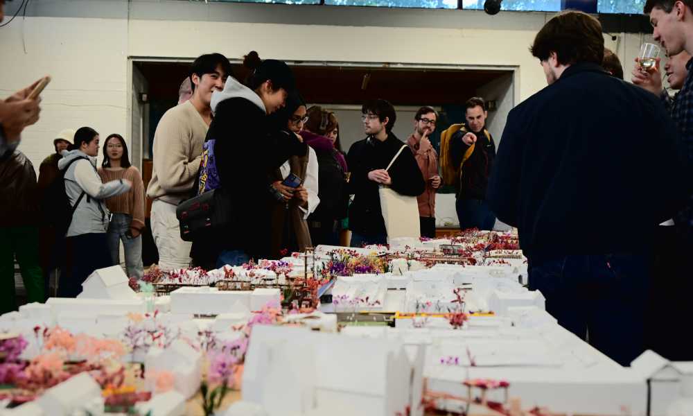 Mixed group of people standing round a table displaying a large architectural model of a town centre