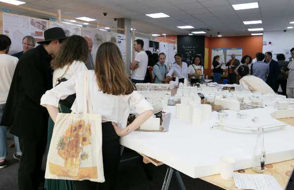 Mixed group of people standing round a table displaying a large architectural model of a town centre