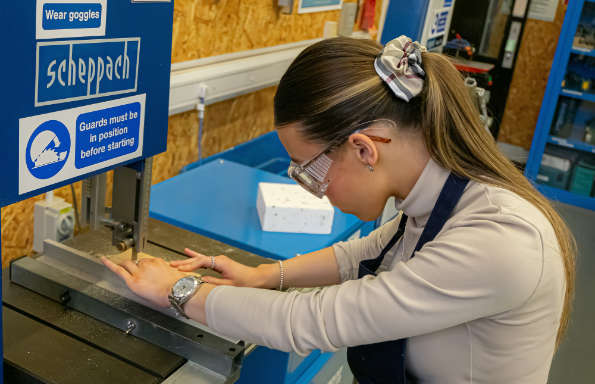 Woman in safety goggles and apron operating a band saw.