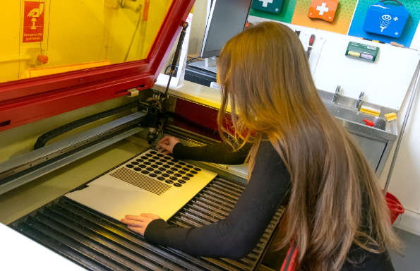 WOman with long hair standing in front of a Laser Cutting Machine, adjusting a p