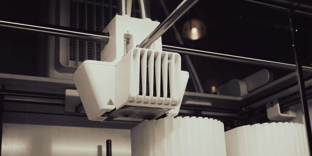 Head of a 3D Printer hovering over two fluted plastic structures being printed.