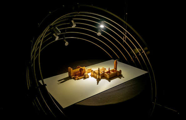 Wooden model of a building illuminated by lights fixed on concentric metal rings.