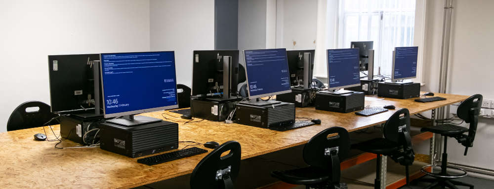 A series of computers sitting on a desk in a computer lab