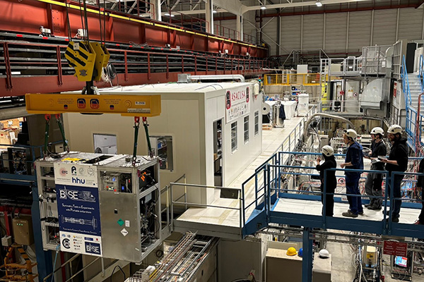 An experiment hall with blocks of concrete and a team looking at a metallic frame being lifted.