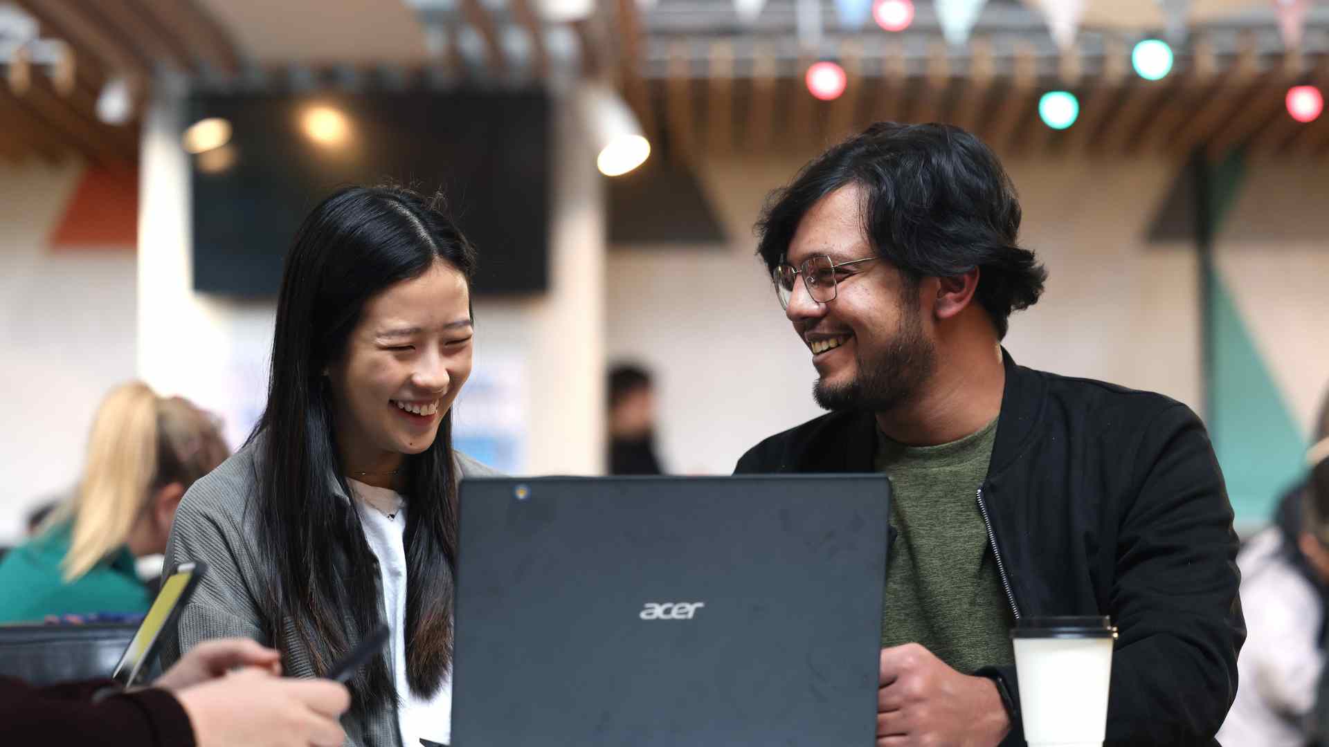 Two graduates looking at a laptop at a cafe