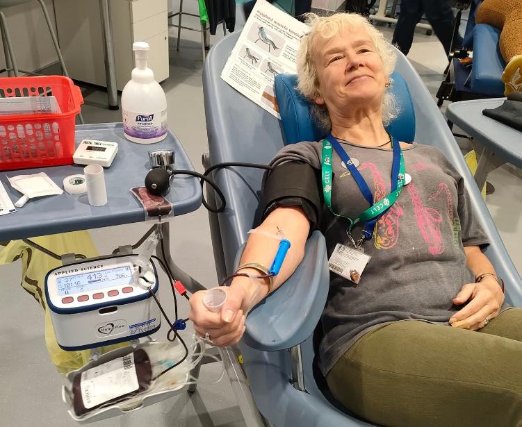 One of CELT's technician is laid back giving blood from their right arm. They have a relaxed smile on their face while they look into the distance