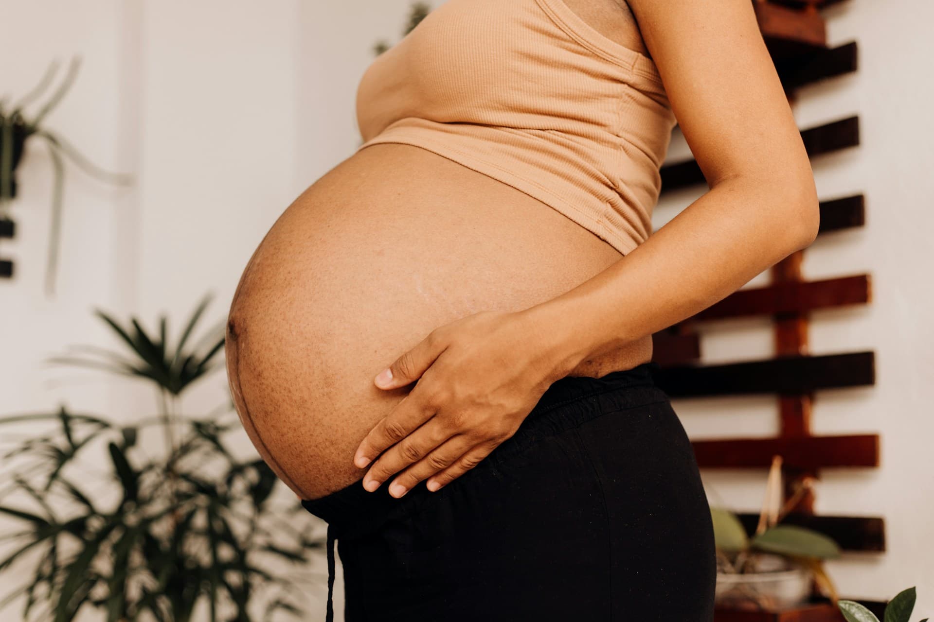 A pregnant woman is stood to the side with their hand on their bump.