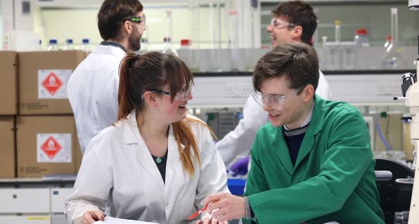Two individuals in lab coats collaborate on a project in a laboratory setting.