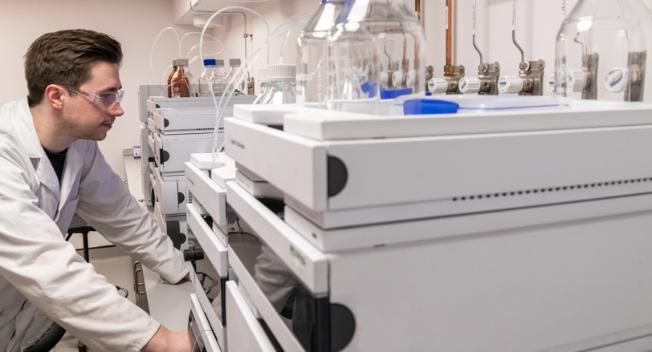 A man in a lab coat operates a complex machine, focused on his work in a laboratory setting.