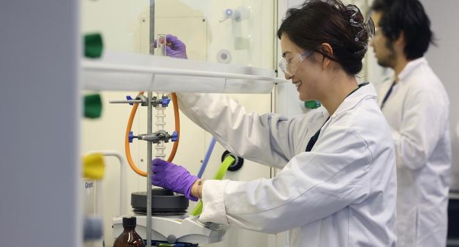 A woman in a lab coat operates a machine, focused on her work in a laboratory setting.