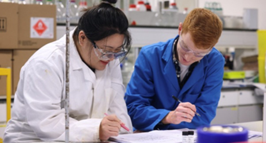 Two students collaborate in a laboratory, focused on their project with lab equipment surrounding them.
