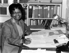 Gladys West pictured sitting at a desk smiling