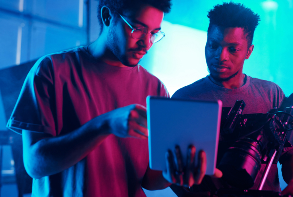 Two students looking at a tablet and holding a camera under neon lighting