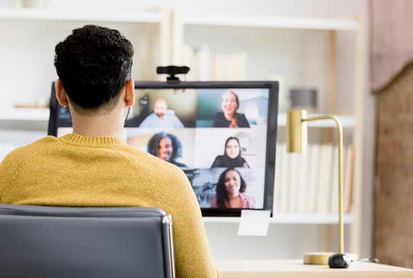 User sitting in front of a screen on a video call showing multiple other team members on the call